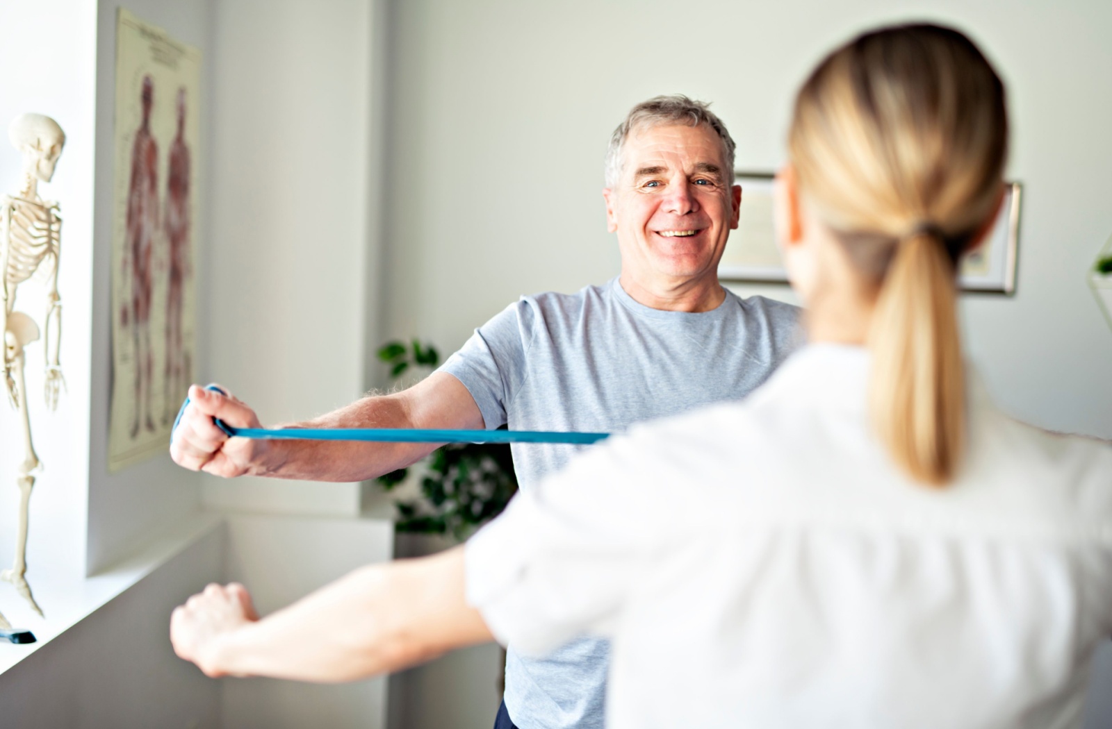 Elderly man exercising with a resistance band under medical supervision.