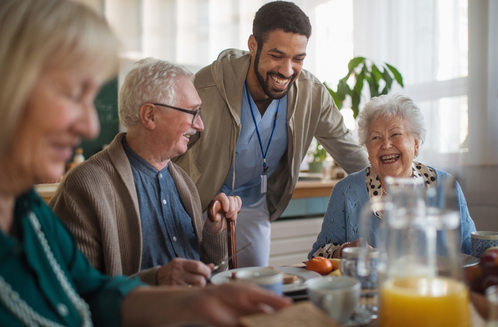 A group of seniors enjoy a healthy breakfast and share a laugh while their nurse checks in on them.