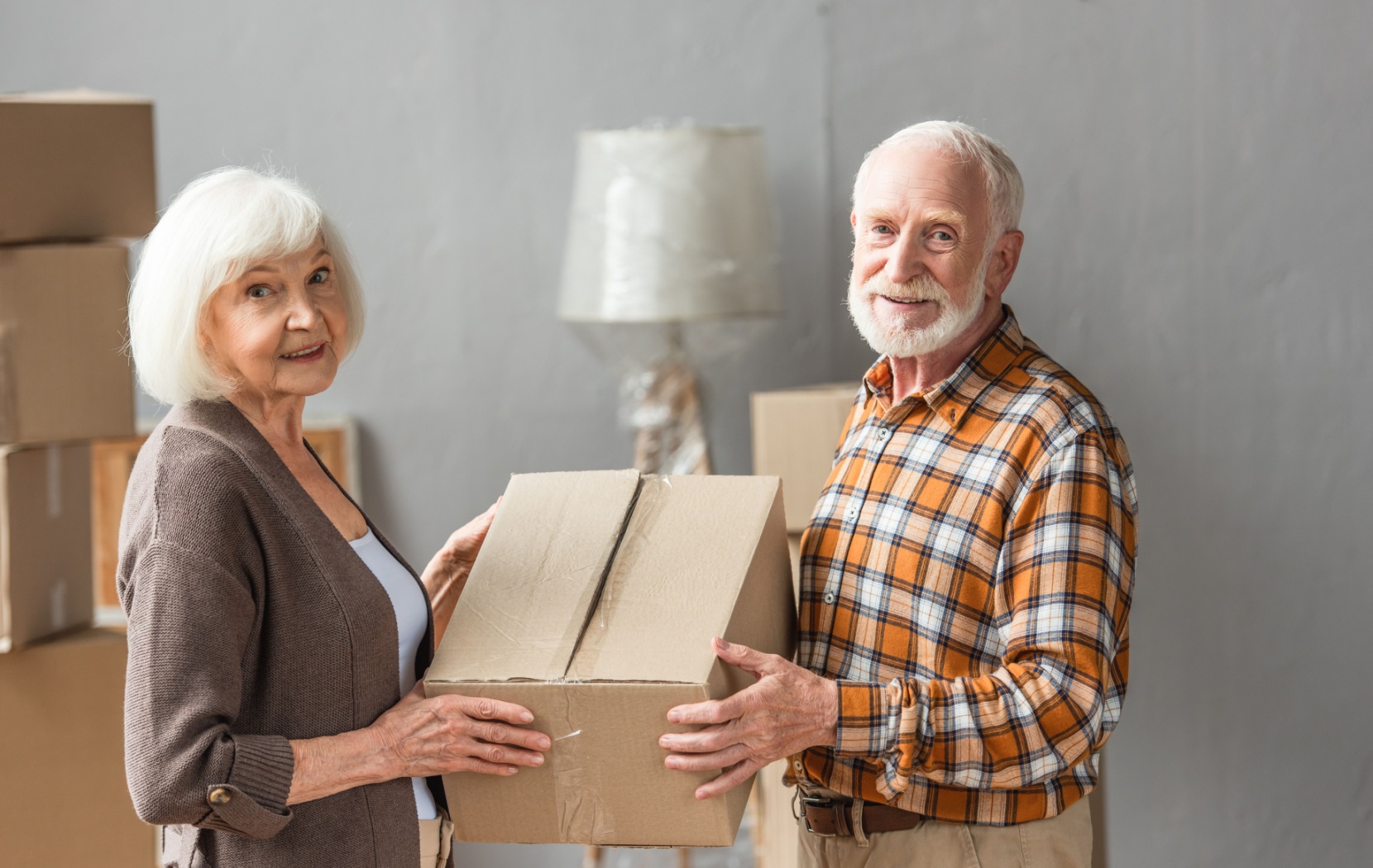 A senior couple smile as they help each other pack and move boxes for their move into a senior living community.