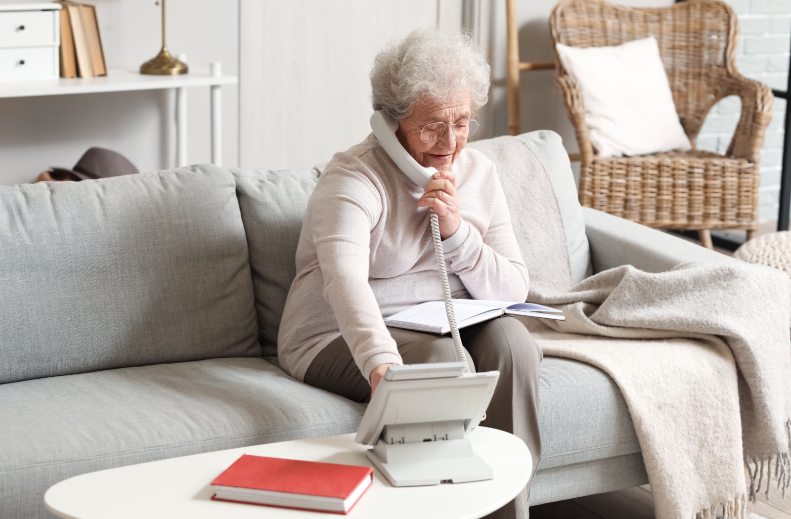 An older adult with dementia smiling in their living room and dialing a number on a landline phone.