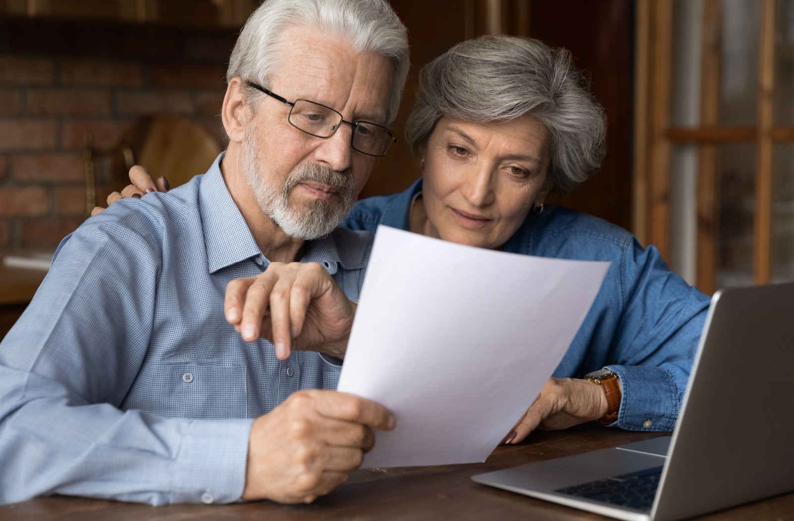 An older couple examining paperwork at their kitchen table to budget for assisted living.