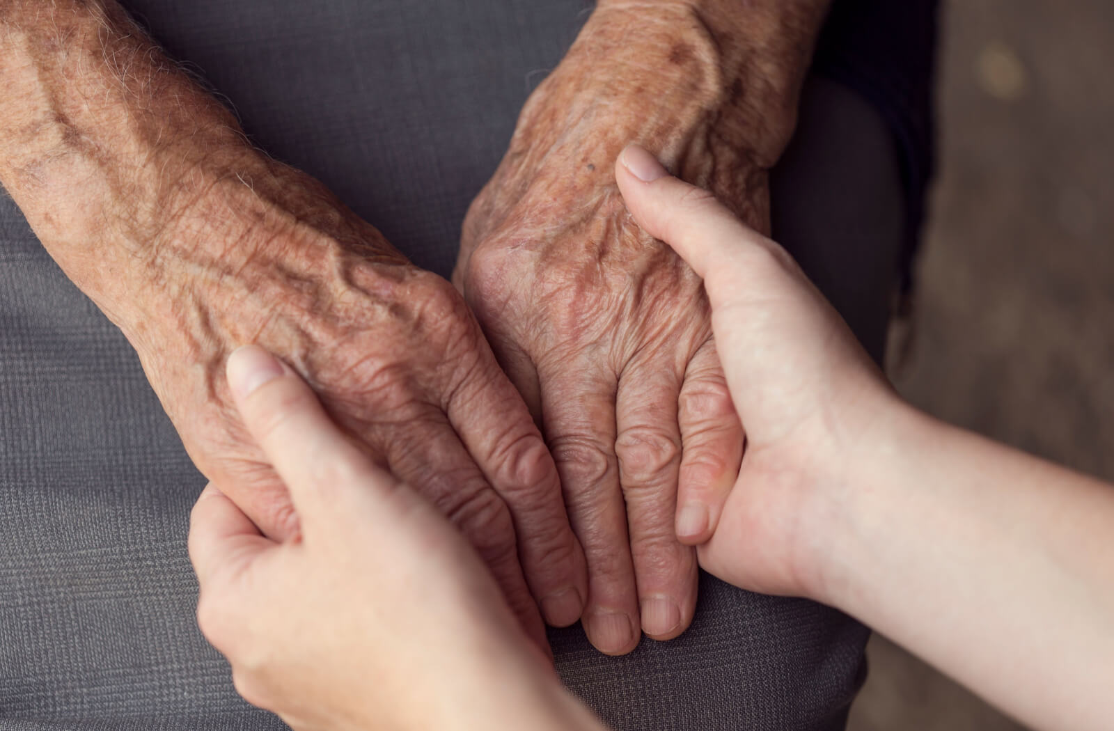A caregiver and an older adult holding hands to support one another.