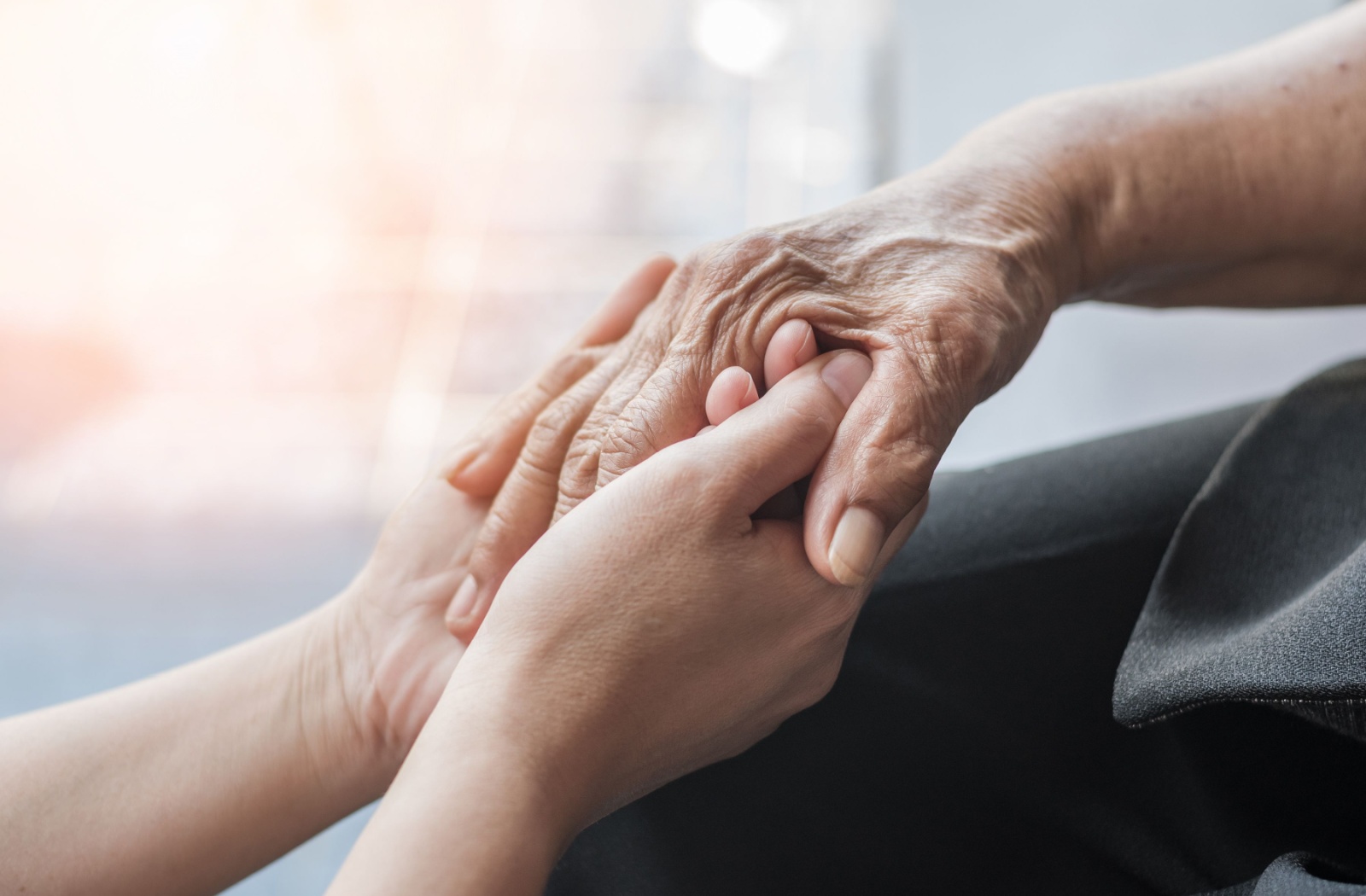 A caregiver clasps the hand of an older adult with Parkinson's while reassuring them