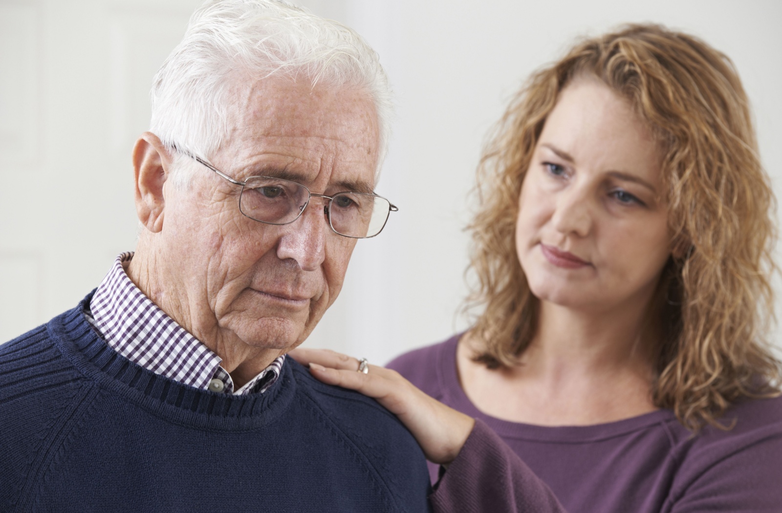 An adult rests their hand on their older parent’s shoulder, expressing concern about their struggle with daily life tasks